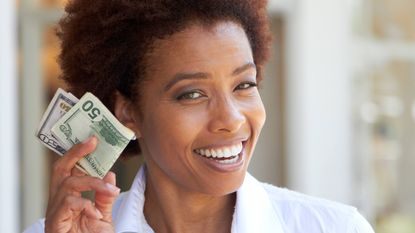 A woman holds up some $50 bills and smiles.