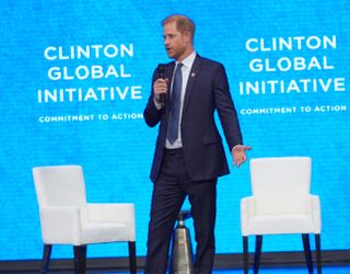 Prince Harry wearing a blue suit and holding a microphone on stage at Clinton Global Initiative event