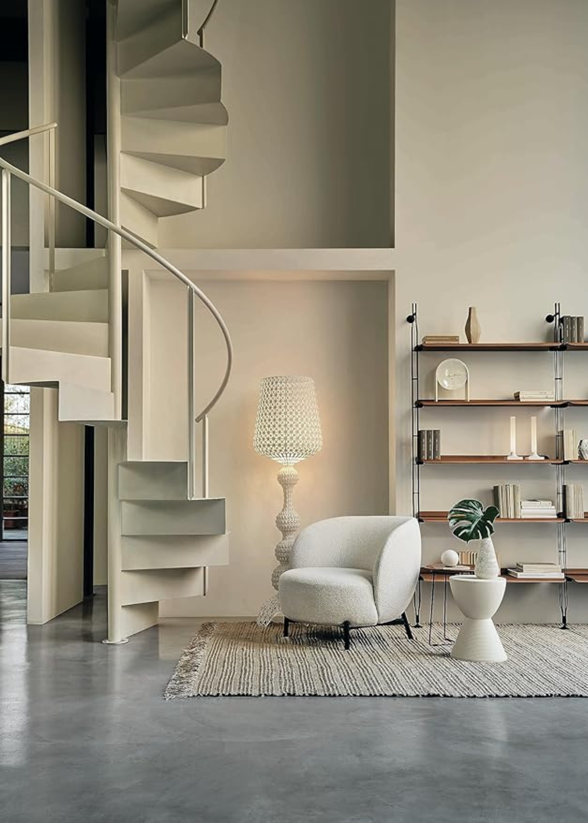 Kartell Prince Aha Furniture white stool at the bottom of a white spiral staircase next to a white accent chair and floor lamp and open shelving