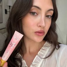 An image of Alyssa Brascia holding and wearing the Supergoop! Glow Gloss SPF 40 Lip Balm.