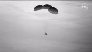 A black and white image of the Boeing Starliner parachuting down from the sky