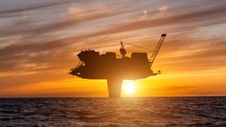 the sun sets behind a large T-shaped drilling platform at sea