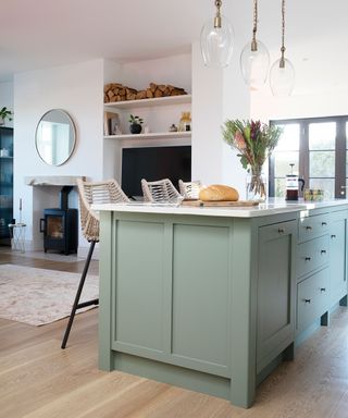 white open plan room with kitchen island in mint green in foreground with kitchen stools and three pendants over the top