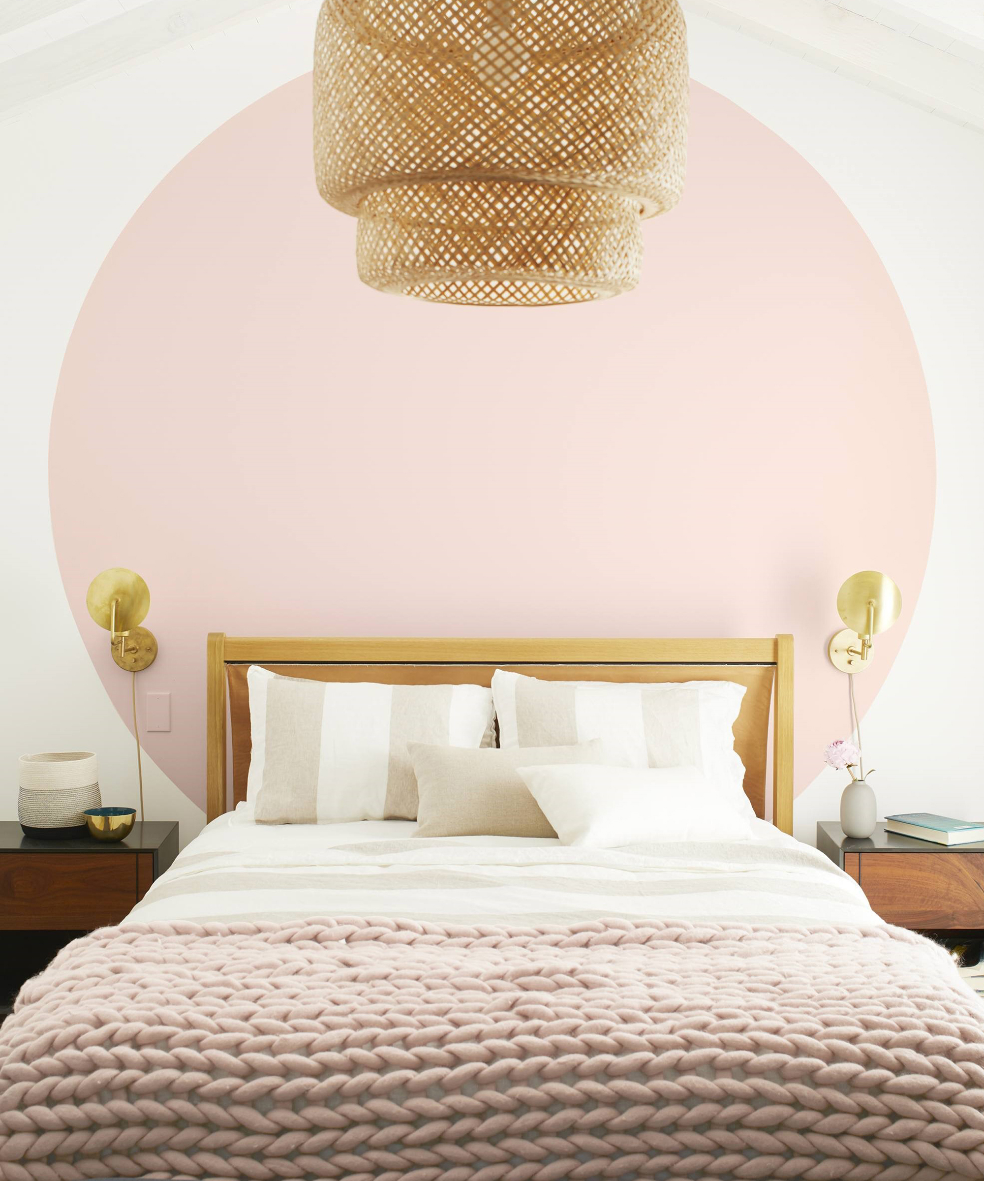 A wooden bed with a pink throw in front of a pink circular wall motif