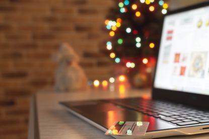 Christmas shopping online. Laptop and credit bank card on table at home on the background of a Christmas tree with blurred bokeh lights.