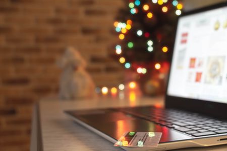 Christmas shopping online. Laptop and credit bank card on table at home on the background of a Christmas tree with blurred bokeh lights.