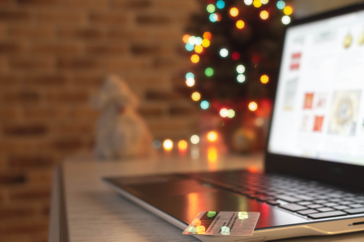 Christmas shopping online. Laptop and credit bank card on table at home on the background of a Christmas tree with blurred bokeh lights.