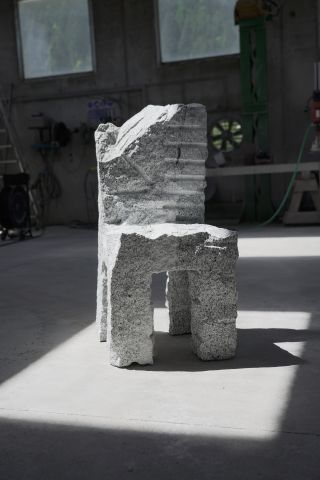 Stone chair shown in the workshop with dramatic light and shadows showing the cuts on the stone resulted from the making process known as feather and wedge