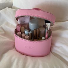 Photo of a full, pink makeup bag resting on a bed 