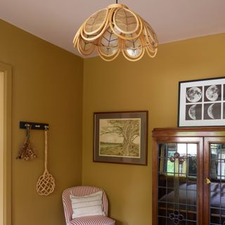 A mustard yellow-painted bedroom with a vintage scalloped ceiling light and a vintage cabinet with stained glass