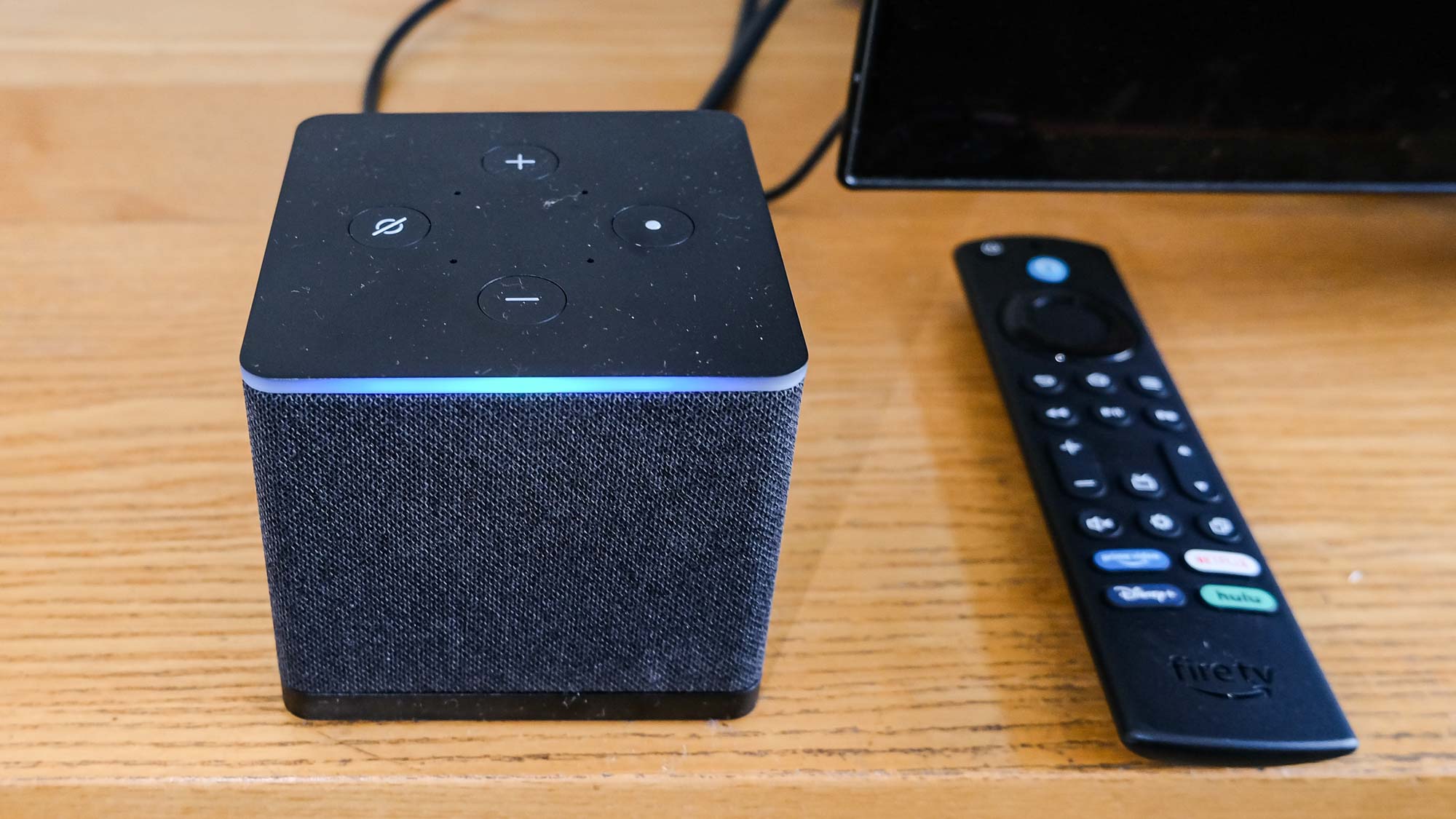Un primer plano del Fire TV Cube (2022) con su barra azul de Alexa brillando y control remoto a la derecha