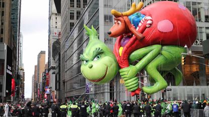A large balloon in the shape of the Grinch carrying a bag of Christmas presents flies at a parade in New York City.