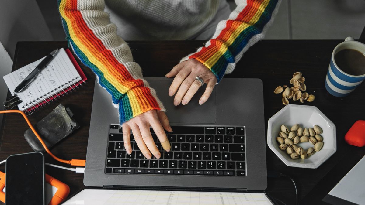 Somebody using a laptop at their desk while wearing a rainbow jumper