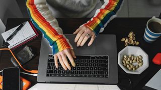 Somebody using a laptop at their desk while wearing a rainbow jumper