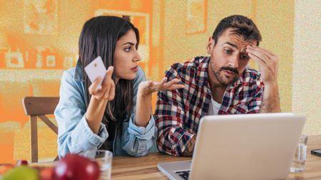 Young couple sitting at a desk in front of a laptop looking concerned.