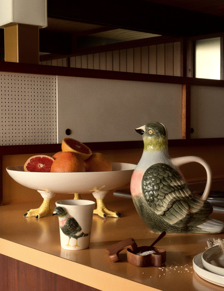 Pigeon-inspired tableware, including a footed bowl, water cup, and pitcher, pictured on a mid-century-style kitchen countertop.