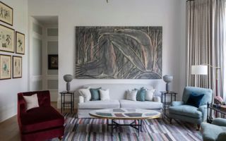 Living room white walls and sofa, artwork, striped rugs and curtains, red velvet accent chair