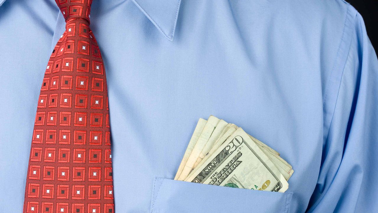 Money pokes out from a man&amp;#039;s dress shirt pocket.