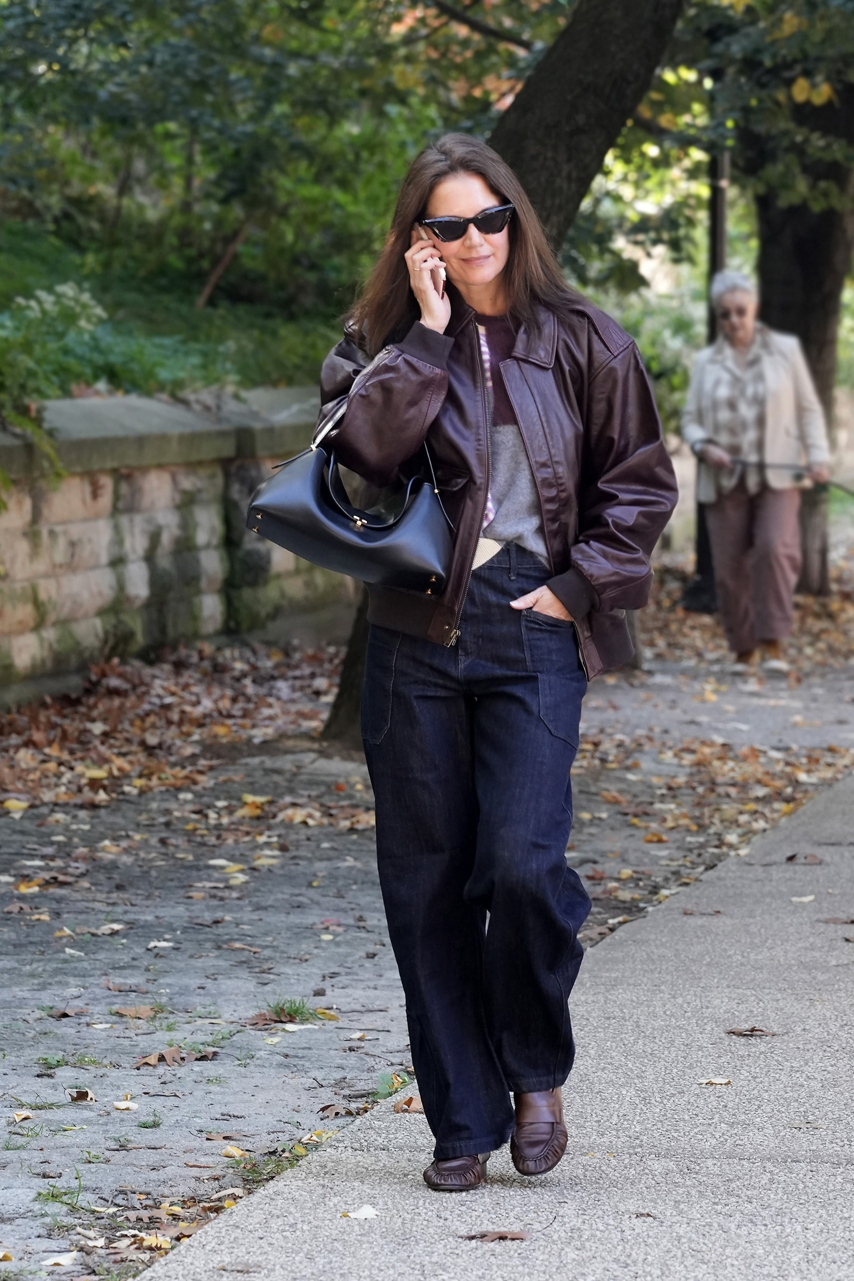 Katie Holmes walks outside on the phone wearing a plum leather jacket with matching loafers and dark wash jeans.