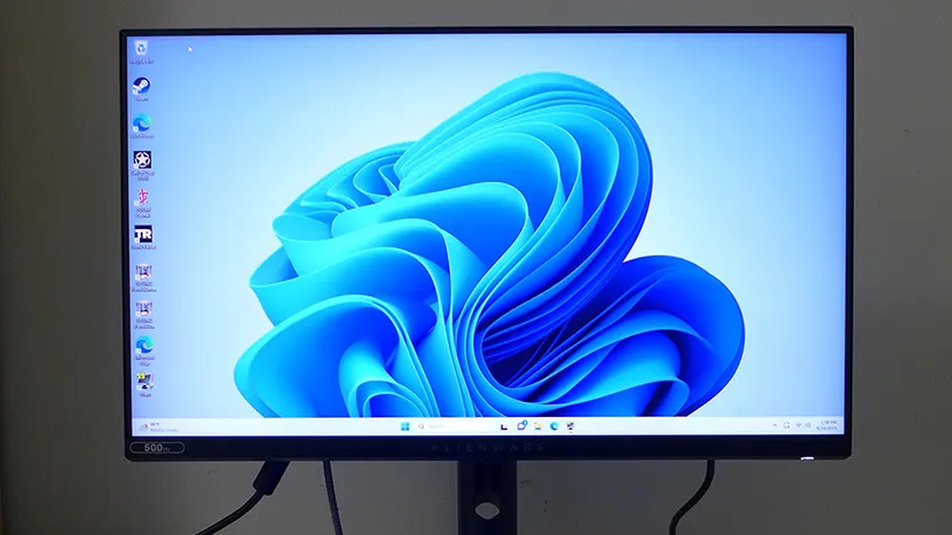 A desktop monitor displays the Windows 11 blue abstract swirl wallpaper, with icons along the left edge and the taskbar below; the clean setup feels modern and calm.