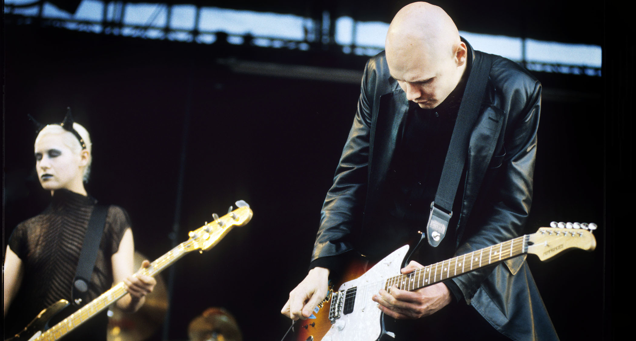 Smashing Pumpkins bassist D&#039;Arcy and frontman Billy Corgan playing a festival date in 1997, with Corgan in a long black leather trench coat, playing an offset.