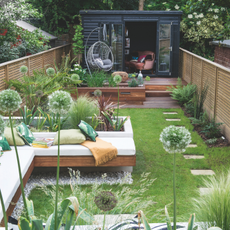 View down the garden with seating area and raised beds, wooden workshop at the end of the garden. The garden of a four bedroom Victorian house in North London, home of Tracey James and Paul Roye and their three adult children.