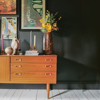 a mid century sideboard against a black wall with a feature wall of wall art