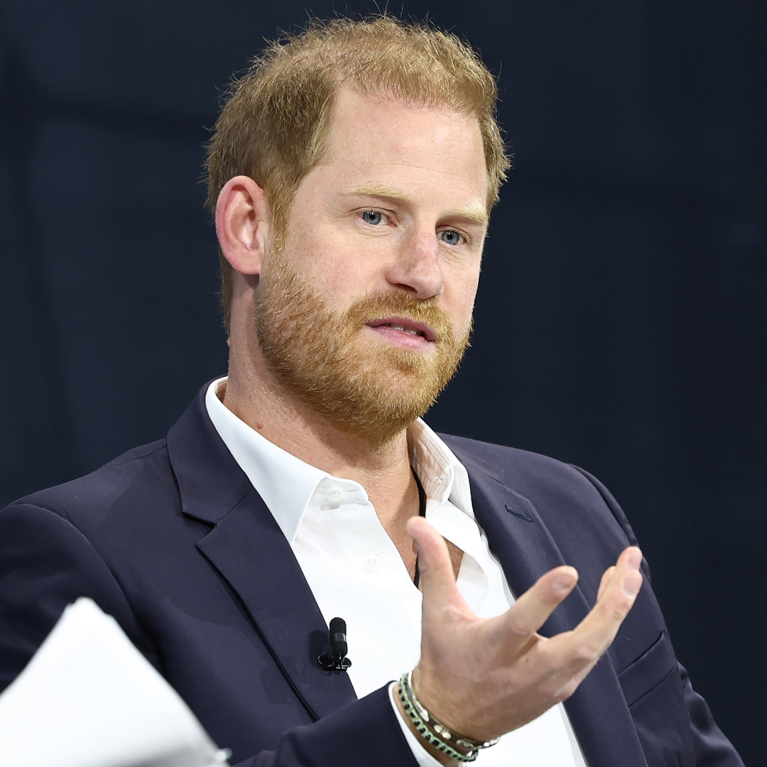 Prince Harry wears a suit with an open white shirt and gesticulates, following news he's offering continued support to a charity beloved by his late mom Princess Diana