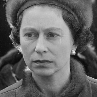 A black and white photo closeup of Queen Elizabeth wearing a fur hat and pearl earrings 