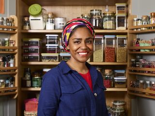 Smiling Nadiya Hussain in front of a wall of spices