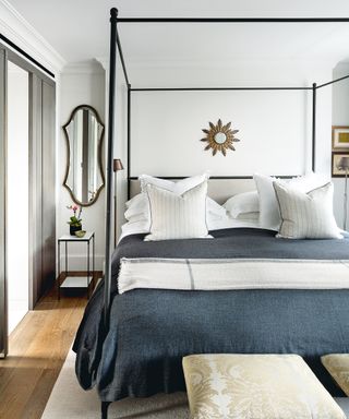 Monochrome simple bedroom ideas in a bedroom with a black four poster bed, white walls, and faded black bed linen.