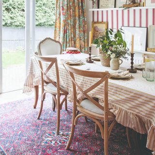 A dining room with a striped wallpaper and tablecloth on the table and a vintage-style ornamental rug underneath