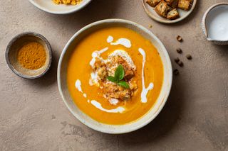 A bowl of carrot, lentil and pumpkin soup with small dollops of cream, and a sprig of basil.