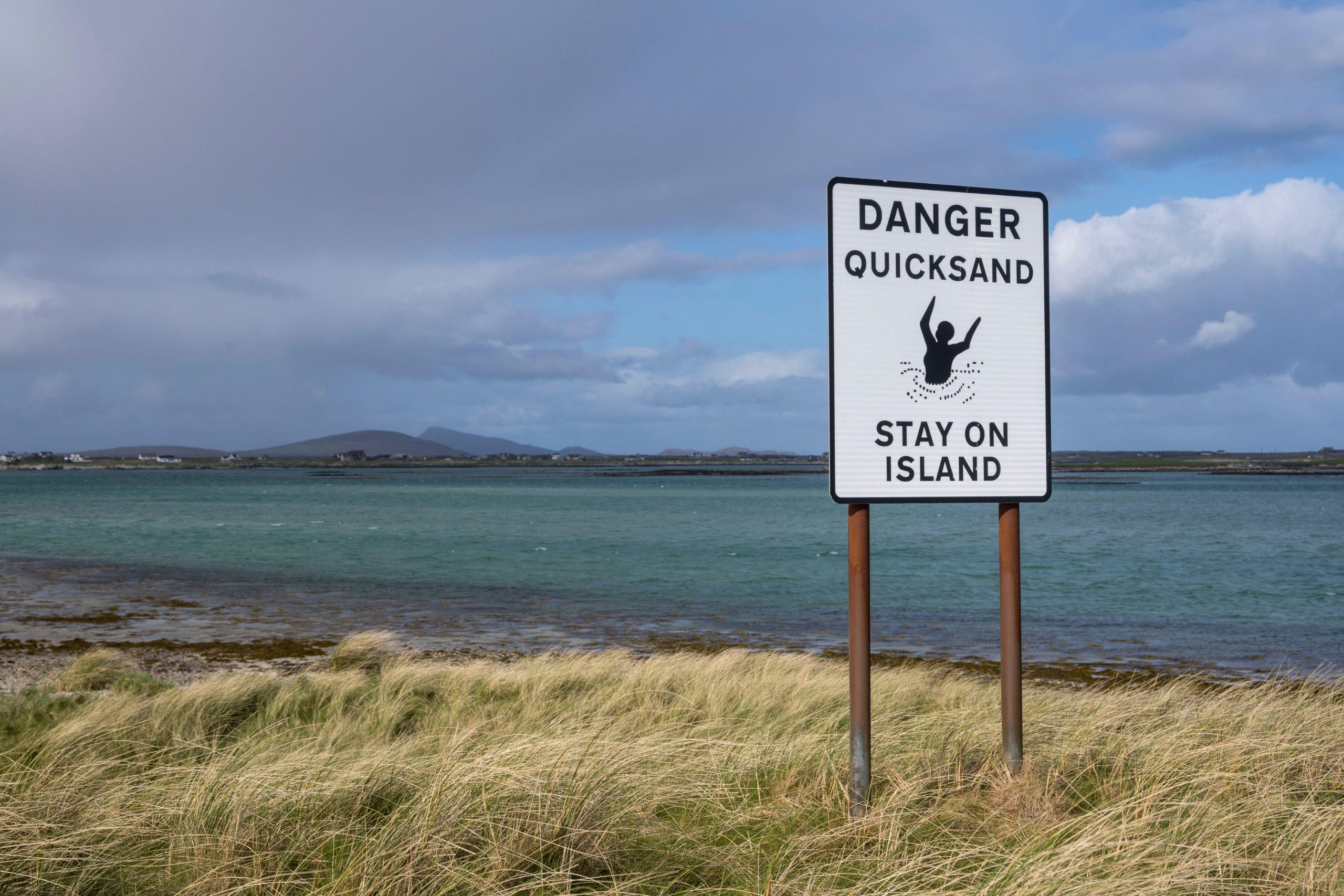 A sign by a beach in scotland, saying 'Danger Quicksand, Stay on Island'