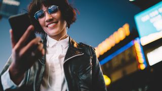 Image of woman wearing sunglasses and wired earbuds looking at her phone