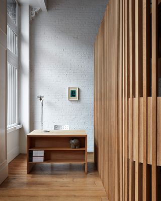 Reception area at Spiral (x,y,z) featuring a white painted brick wall, partition made from wood slats, oak desk with shelving and chair by a large window
