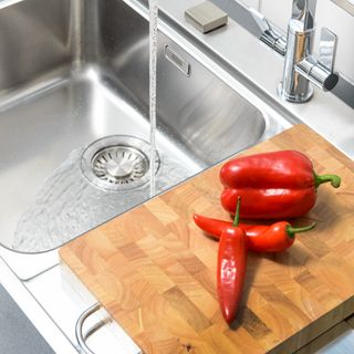 Peppers on wooden chopping board next to stainless steel kitchen sink