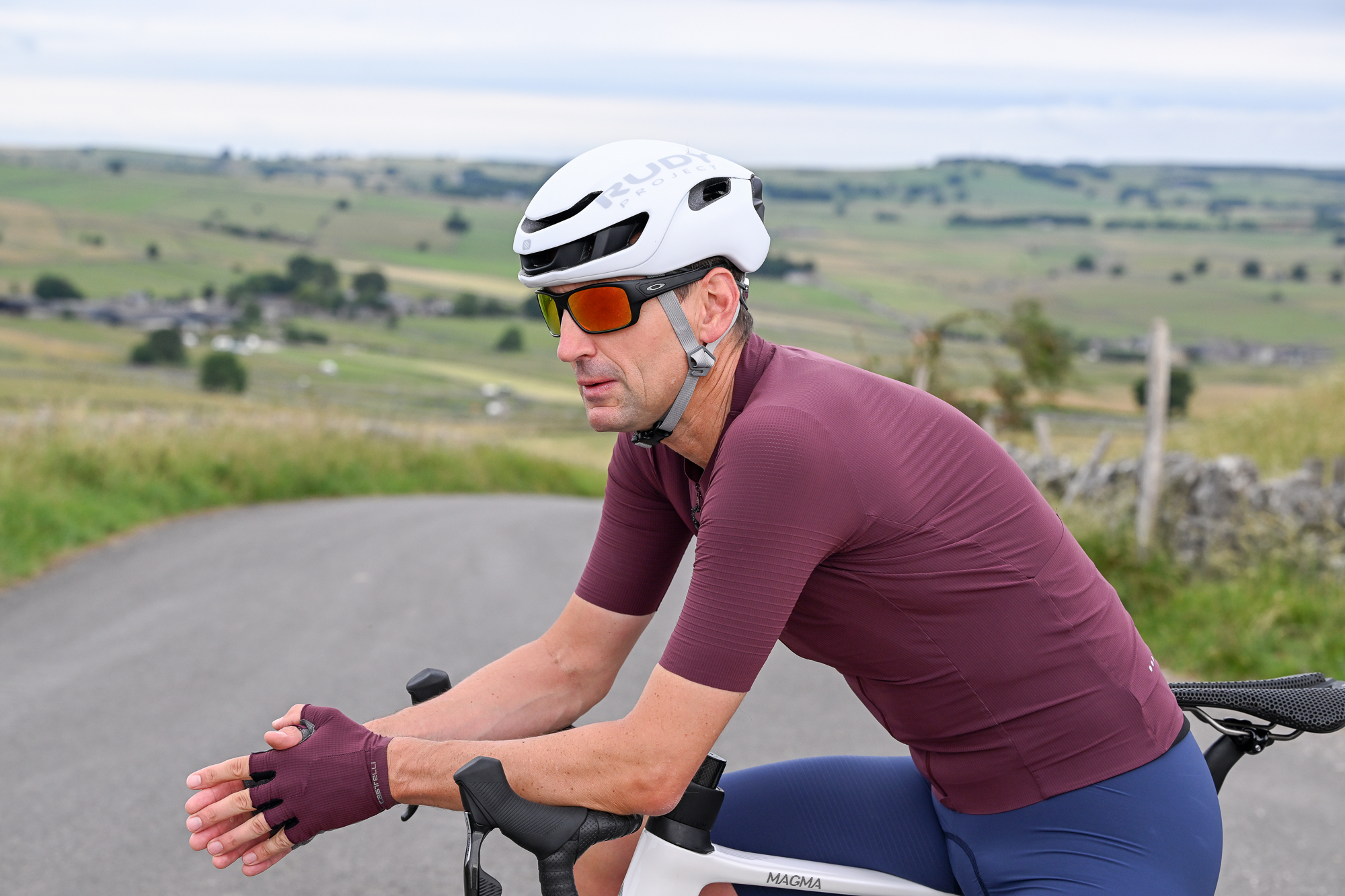 Man wearing a purple jersey, blue cycling shorts and a white helmet sitting on a bike's top tube