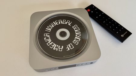 Top-down image of the Fosi Audio Merak CD player, playing a Universal Sounds of America compilation CD, with a remote control on a white background.