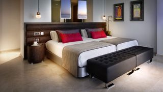 Hard Rock Hotel room, Neytral meable floor, two sinlge beds set together, large brown padded headboard, white covers, brown throws and red cushions, white walls, pictures framed, ceiling lights, two mirrors reflecting the sea view, padded leather bench seating at the end of the bed