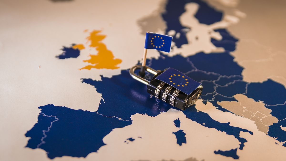 A map of the European Union, coloured in dark blue with white borders between the countries, with a number combination padlock laid on top of eastern France, northern Italy, Switzerland, Belgium, and Luxembourg. The padlock has a sticker of the EU flag on it, with another EU flag on a small wooden stick holding it in place.