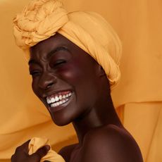 Portrait of smiling young black woman wearing yellow headscarf wearing a cream blusher