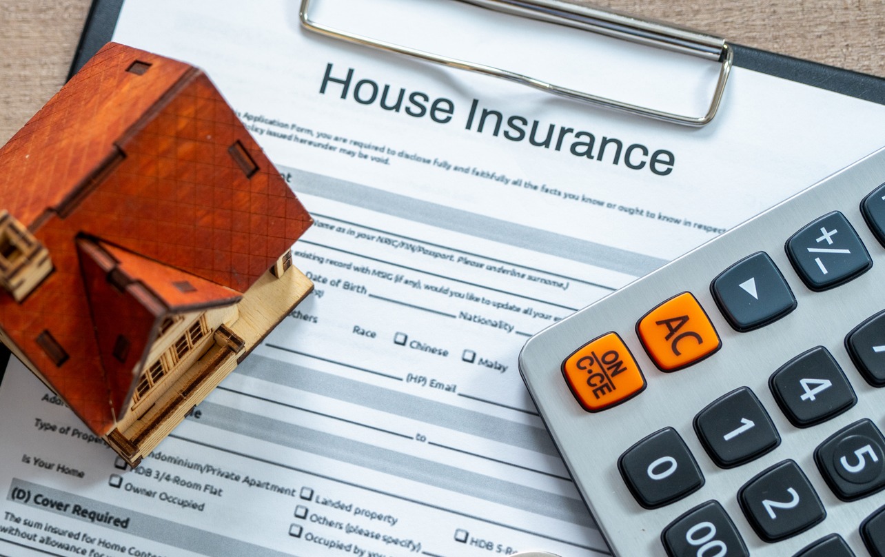 A home insurance application on a desk, next to a calculator and small model home.