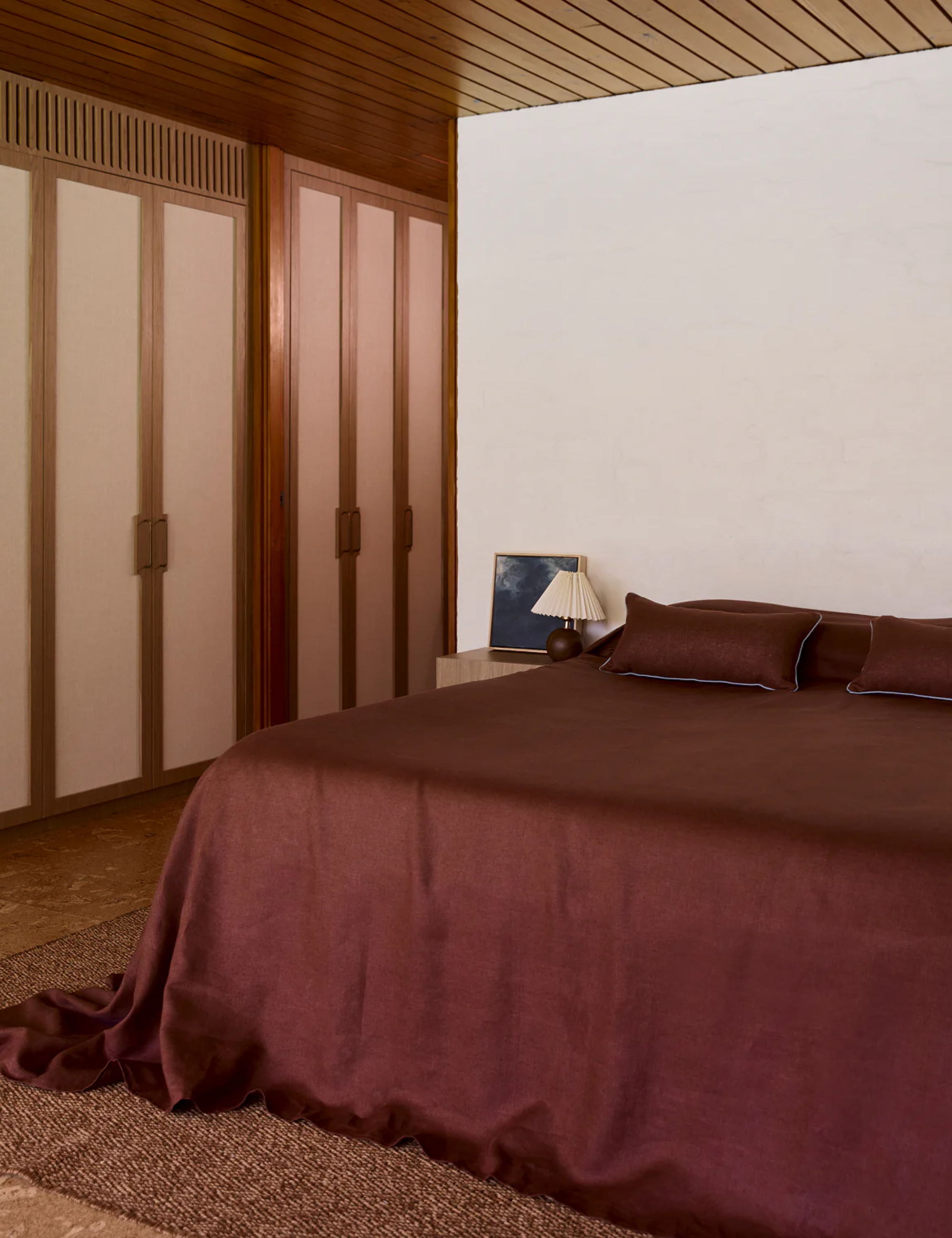 Warm minimalist bedroom featuring a platform bed dressed with chocolate brown linen bedding piped with sky blue.