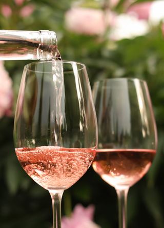 A person pouring rose wine from bottle into glass against beautiful peonies