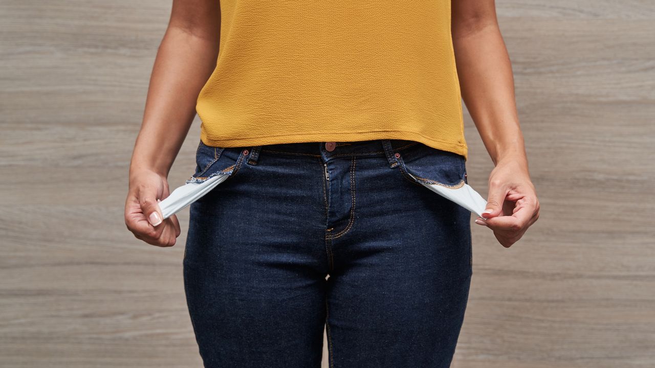 A woman pulls out the pockets of her pants, showing that they&#039;re empty.