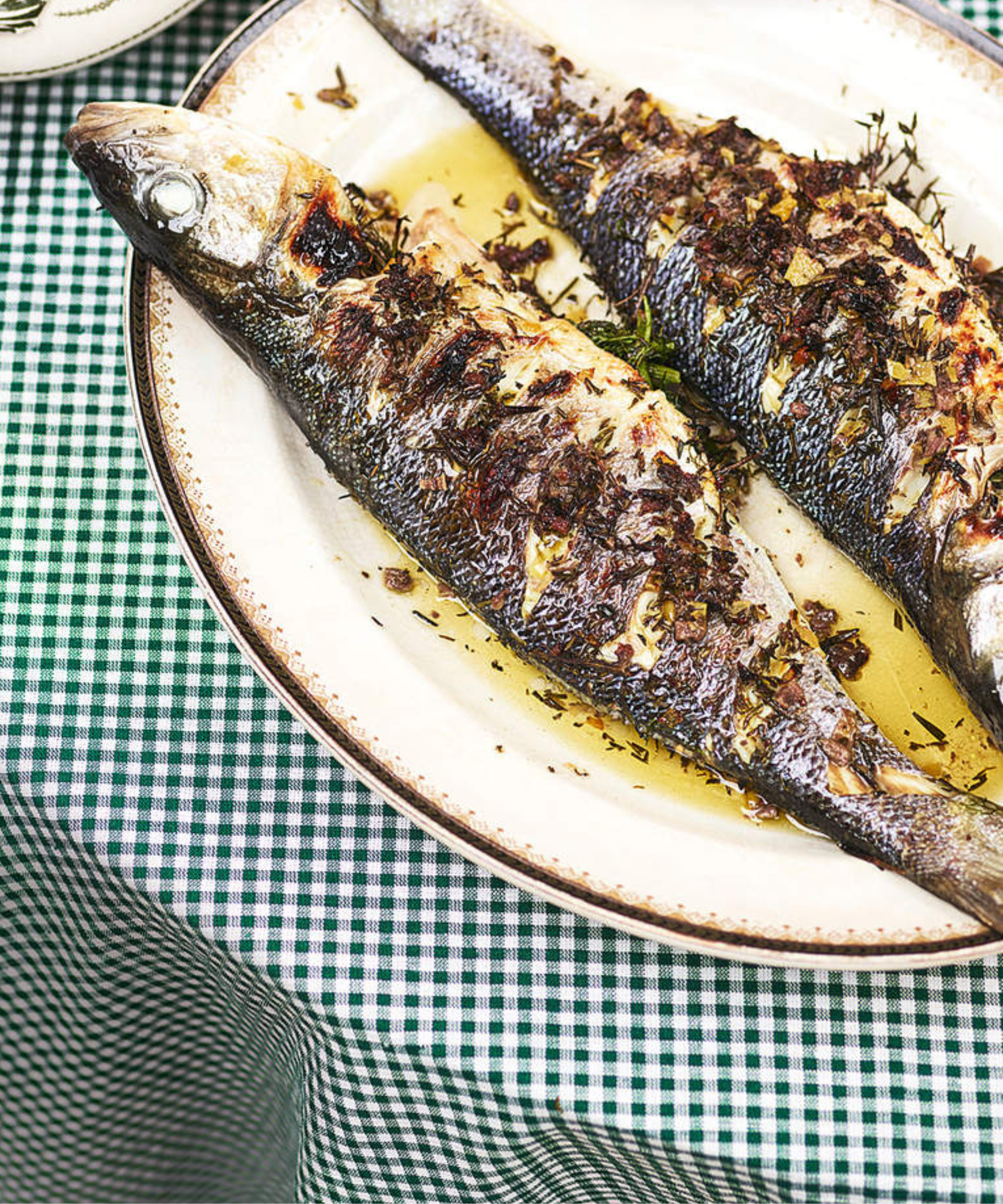 A dish of grilled sardines on a gingham tablecloth