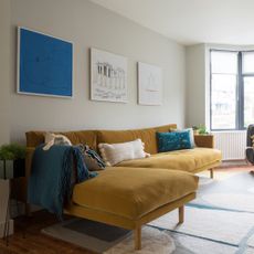 An off white-painted living room with a mustard yellow chaise sofa with the front legs on top of a graphic rug