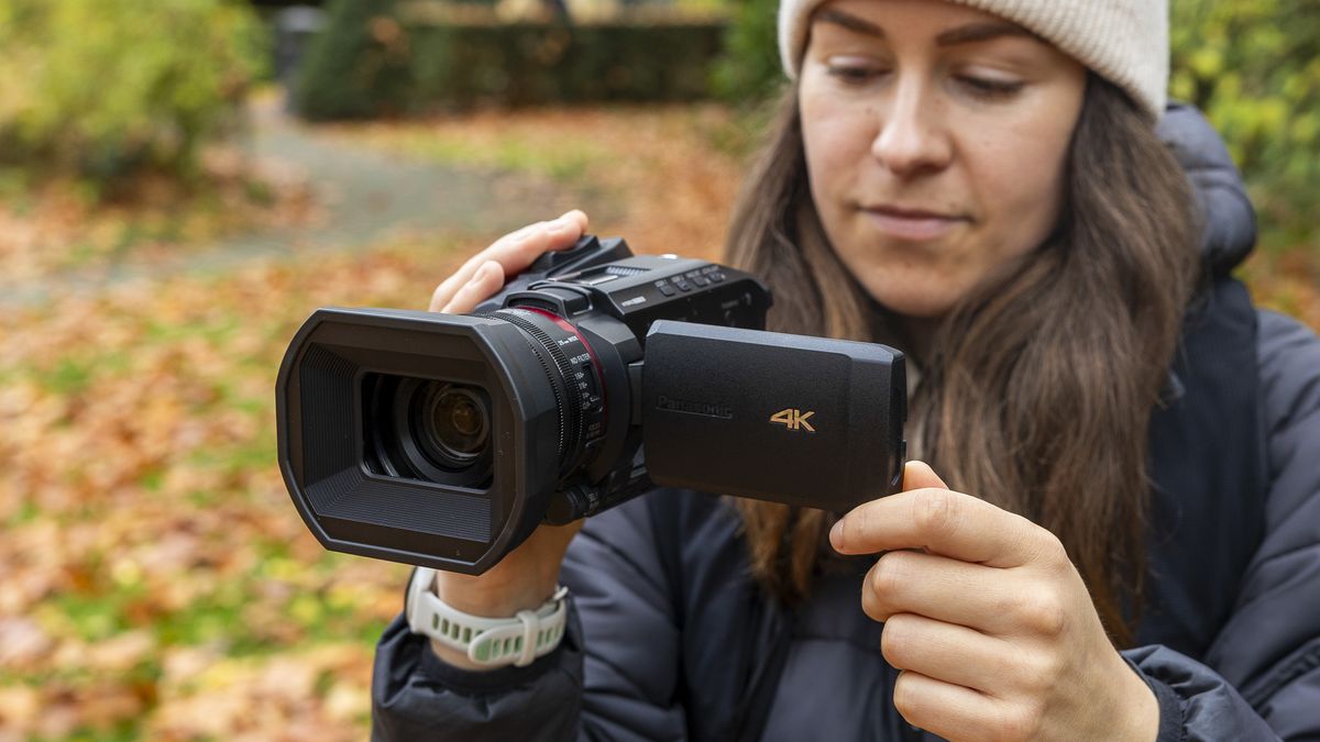 A female photographer holding the Panasonic HC-X1200 in an autumnal scene