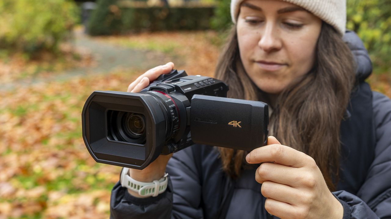 A female photographer holding the Panasonic HC-X1200 in an autumnal scene